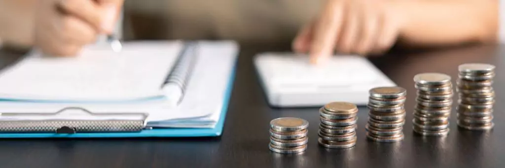 mulher fazendo contas e pilha de moedas à frente